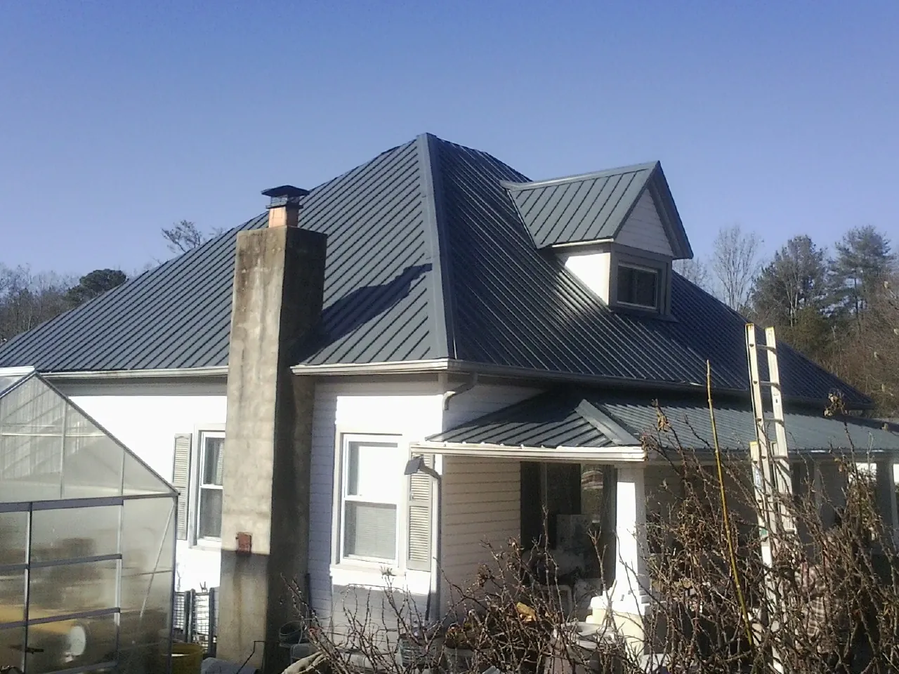 Dark blue standing seam metal roof on a white farmhouse with dormer — Slate & Tile Roof Repair by Roofing Brothers in Port Edwards