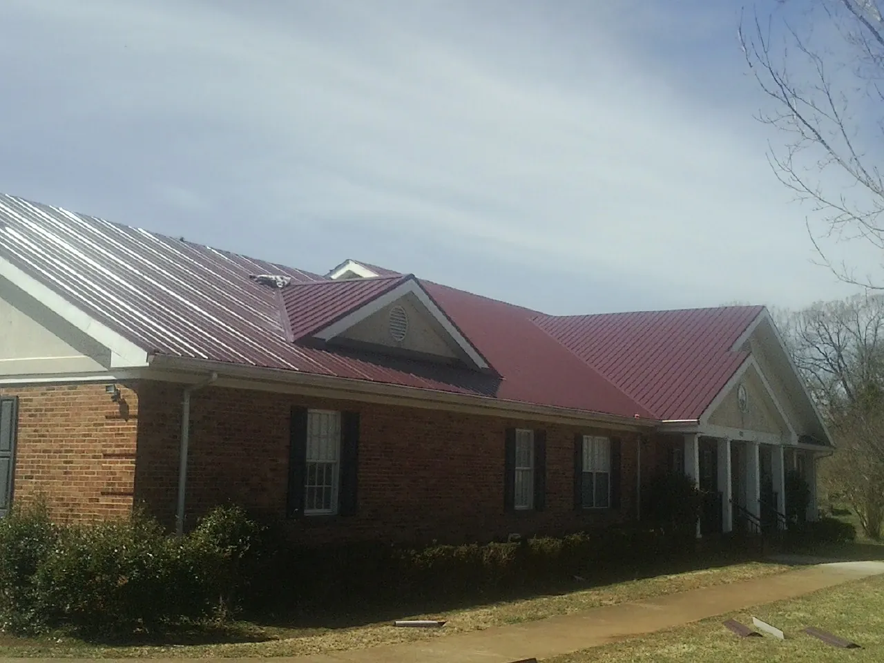 Red metal roof with gabled entries on a long brick building, from a Hail Damage Roof Repair job in Port Edwards