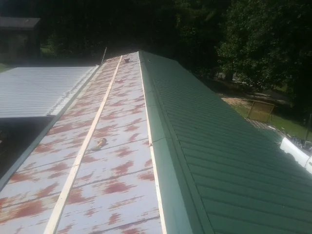 Old rusted panels beside newly installed green metal roofing — Wind Damage Roof Repair by Roofing Brothers in Port Edwards