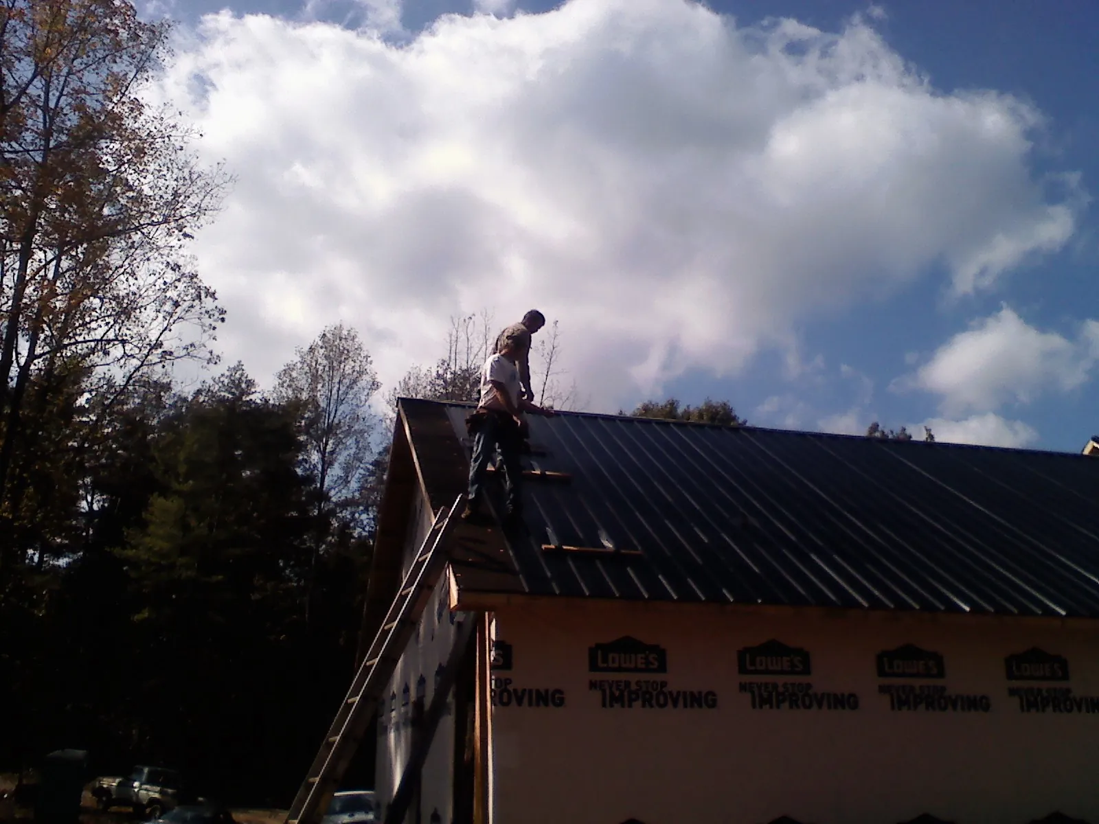 Roofer fastening dark metal panels high against a cloudy sky, from a Roof Inspection job in Port Edwards