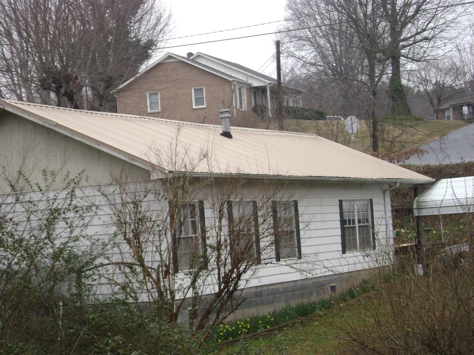 Tan metal roof on a white sided house set into a hillside — Commercial Roofing by Roofing Brothers in Port Edwards
